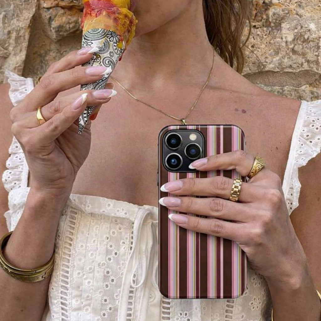 Person holding a phone with a striped case and an ice cream cone, wearing a white lace top.