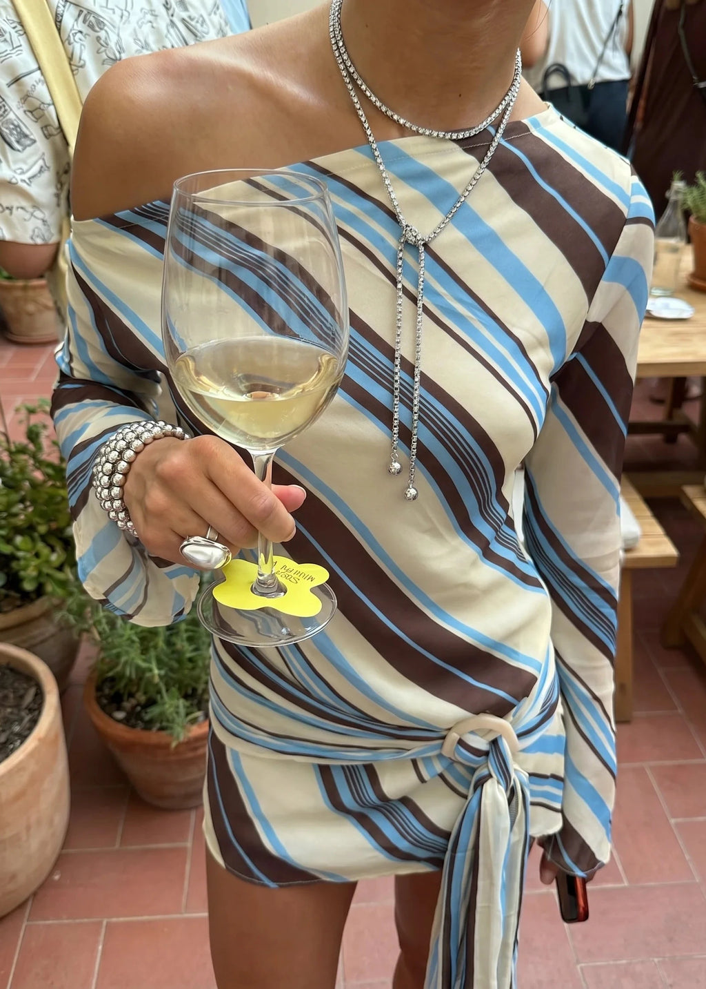 Person wearing a striped dress holding a glass of white wine with a decorative coaster.