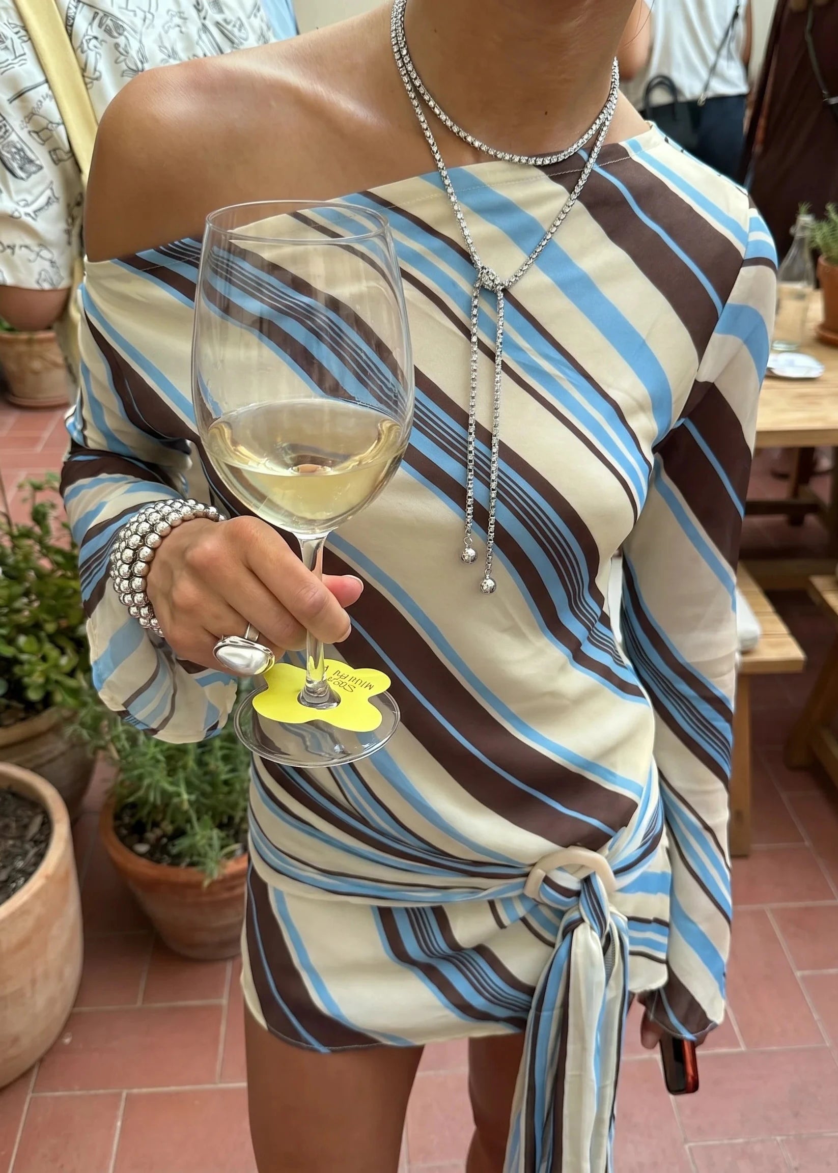 Person wearing a striped dress holding a glass of white wine with a decorative coaster.