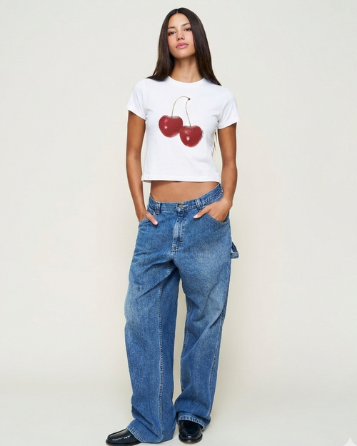 Woman wearing a white t-shirt with red cherries and blue jeans on a plain background