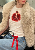 Person wearing a fluffy beige coat over a white shirt with a red fruit design, standing in a store.
