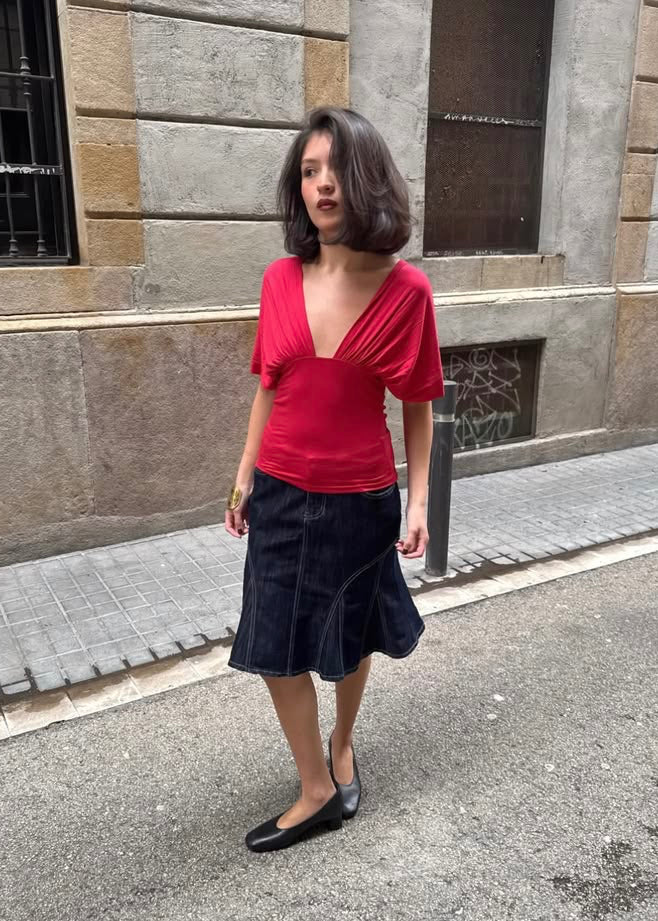 Woman in a red top and black skirt standing on a street with a building in the background