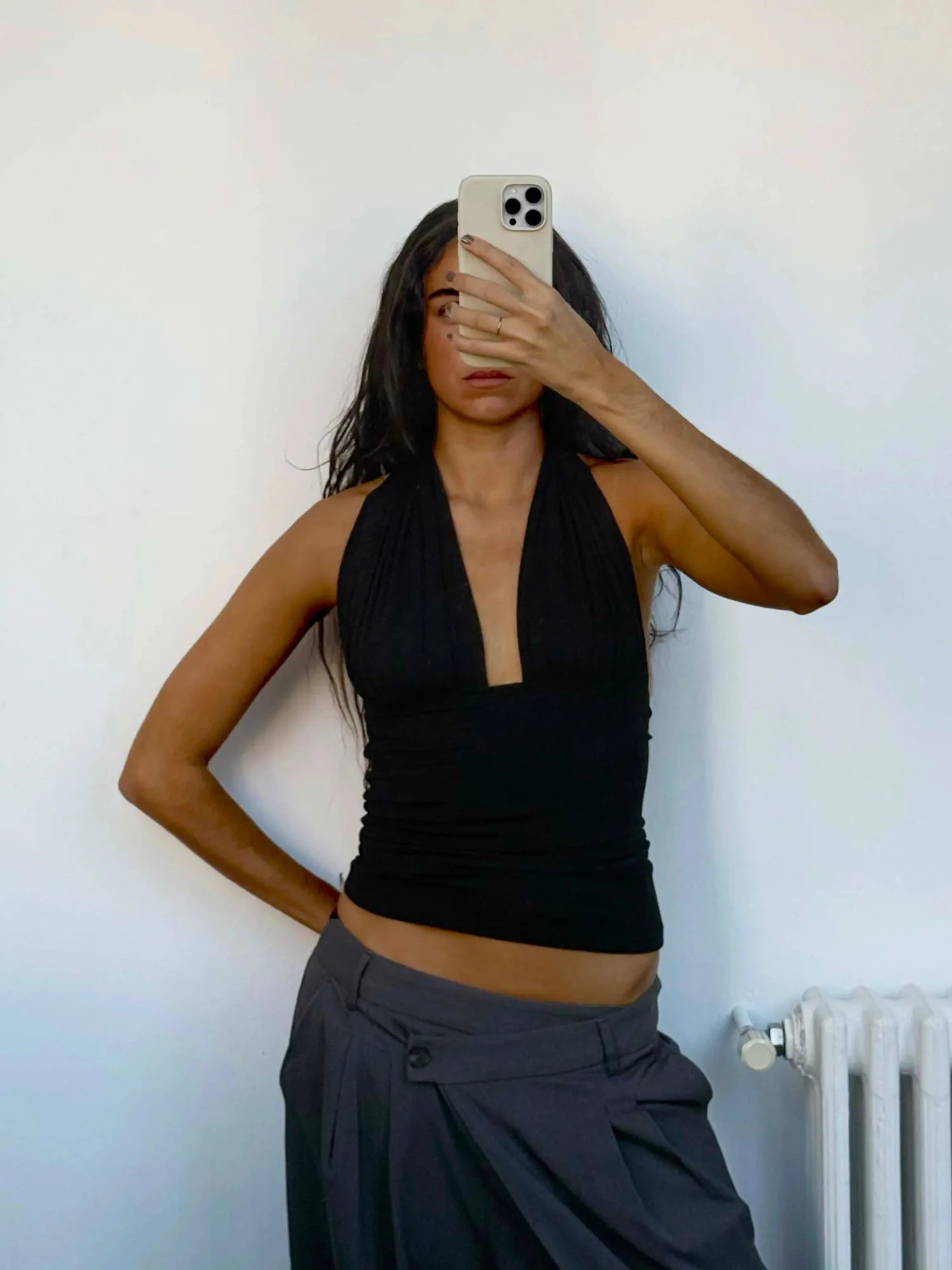 Person wearing a black halter top and gray pants against a white wall.