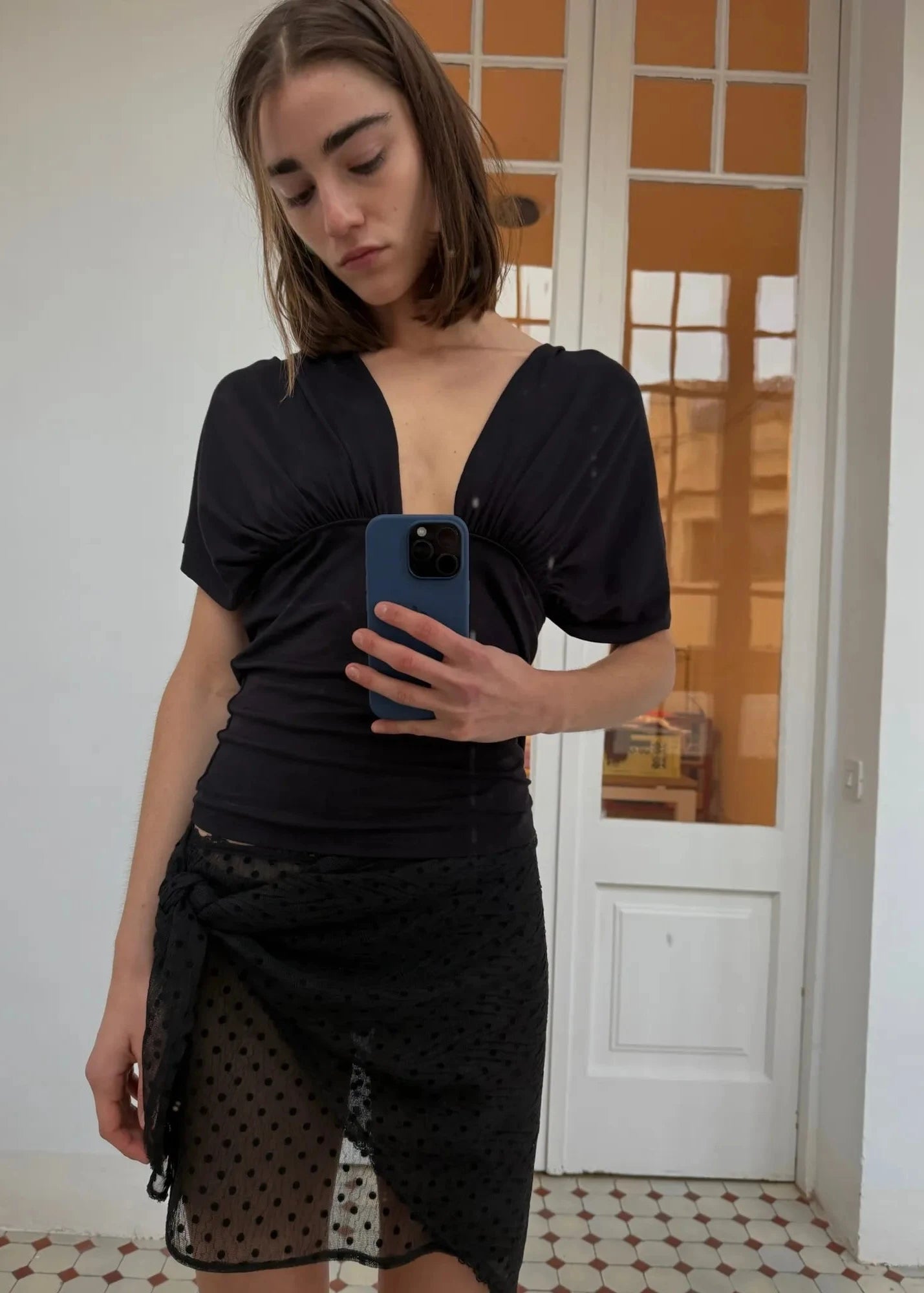 Woman taking a mirror selfie wearing a black outfit with sheer details.