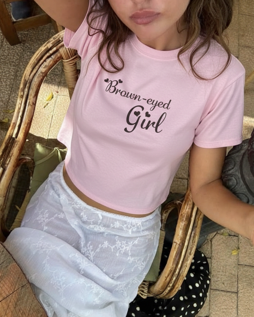 Person wearing a pink t-shirt with 'Brown-eyed Girl' text, sitting outdoors.