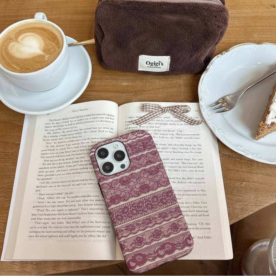 Café au lait, cake, phone with patterned case, book, and brown bag on a wooden table.