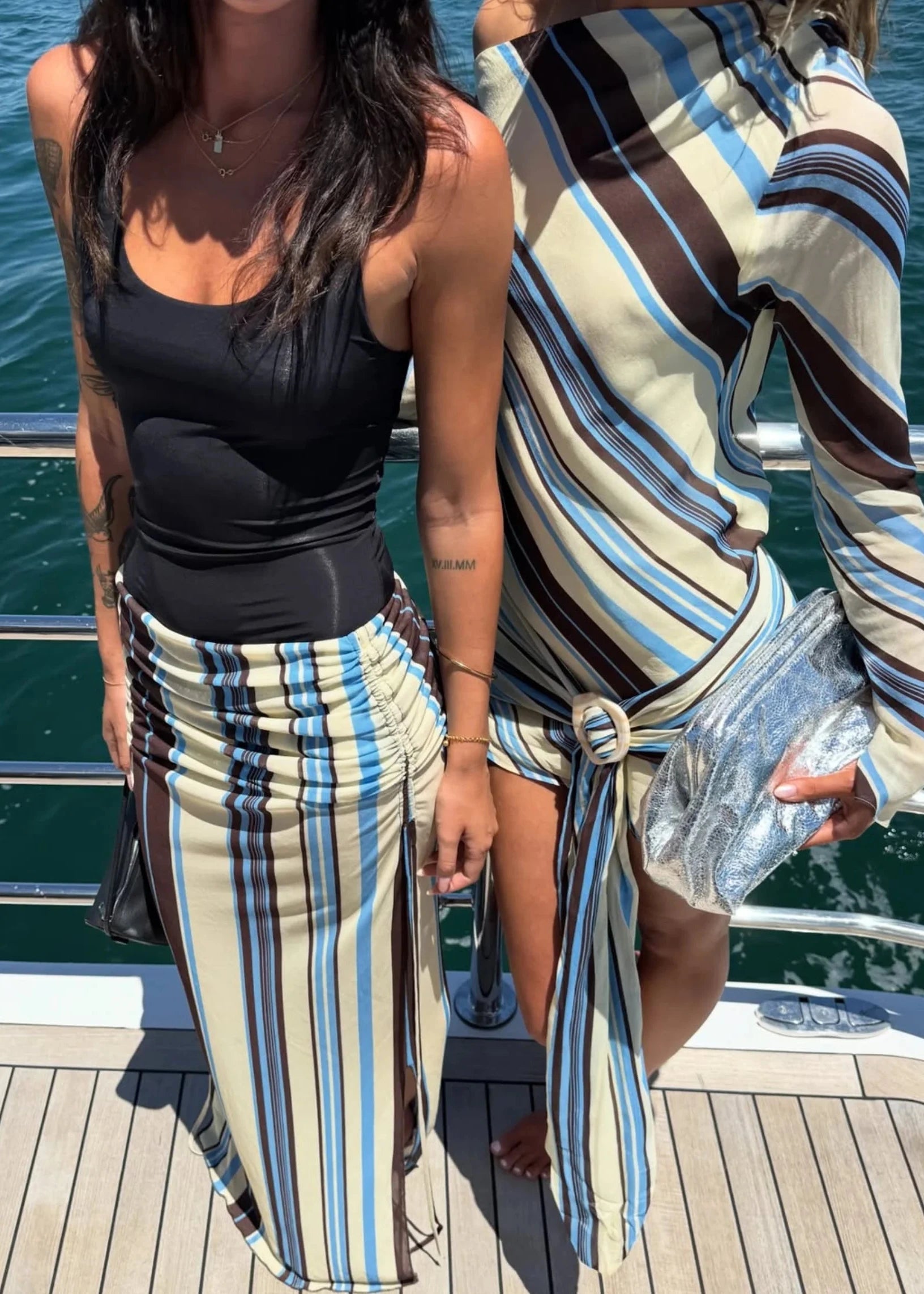 Two women on a dock wearing matching striped outfits with water in the background.