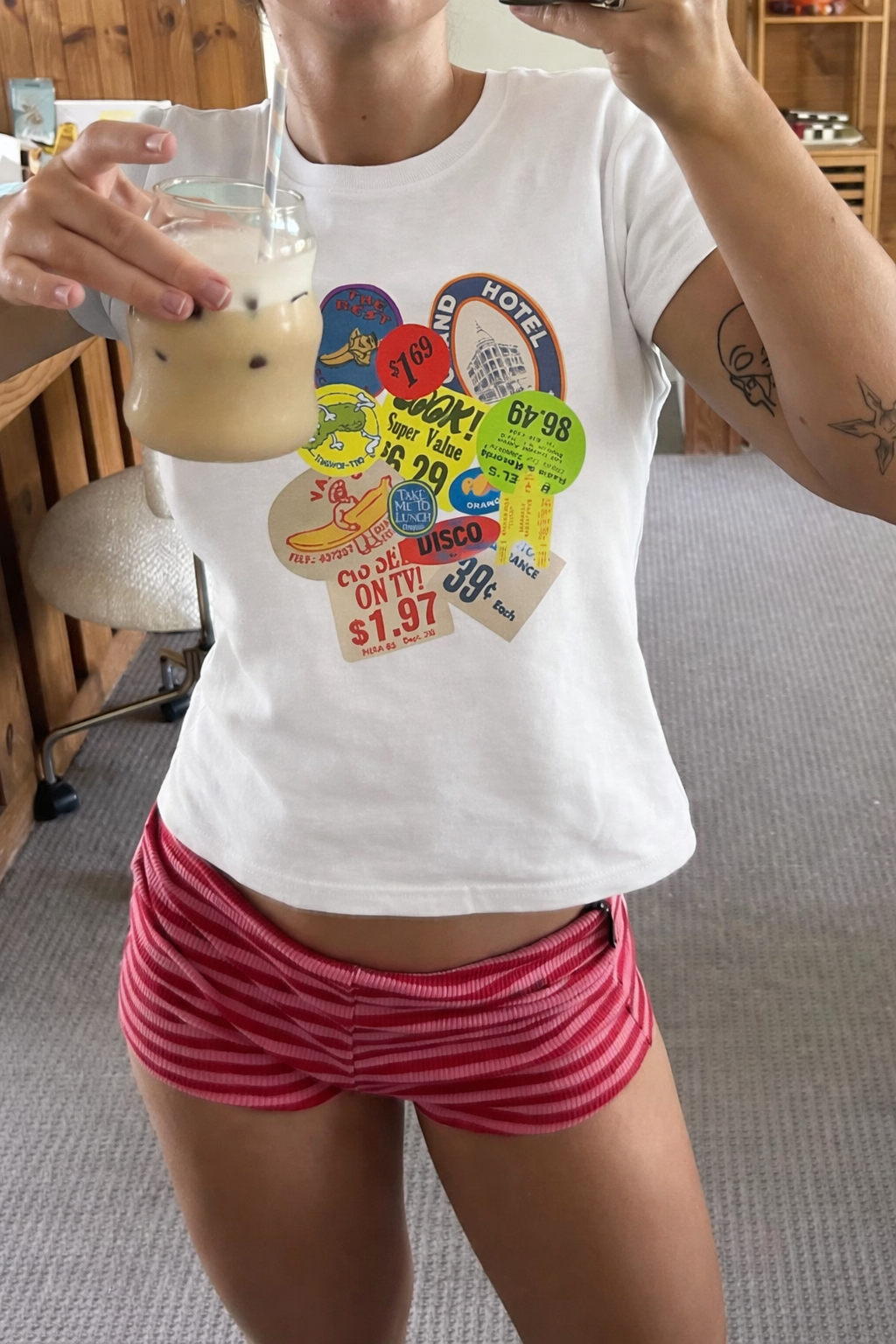 Person wearing a white t-shirt with colorful graphics and pink shorts, holding a glass of milk.