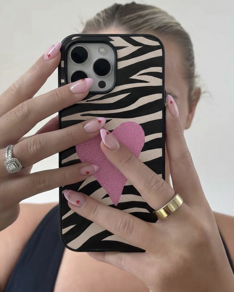 Person holding a phone with a zebra pattern case and pink heart charm.